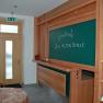 Interior view of a hotel with a board reading 'Gasthof Zur Alten Schule' and a shelf with brochures.