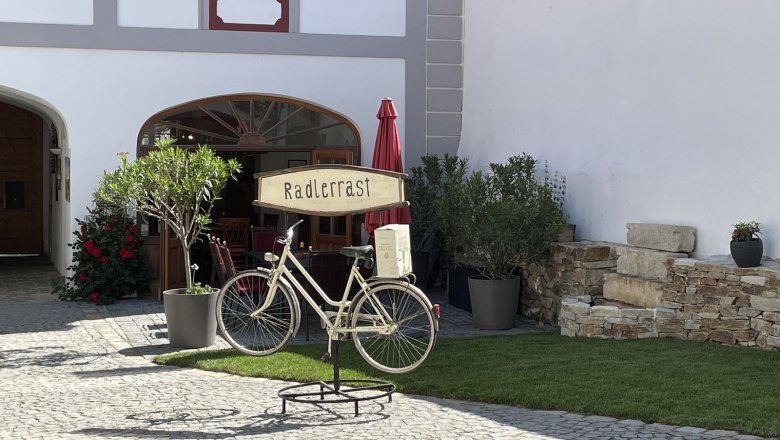 A decorative bicycle with a "cyclists' rest" sign stands in front of a building with plants and a parasol.