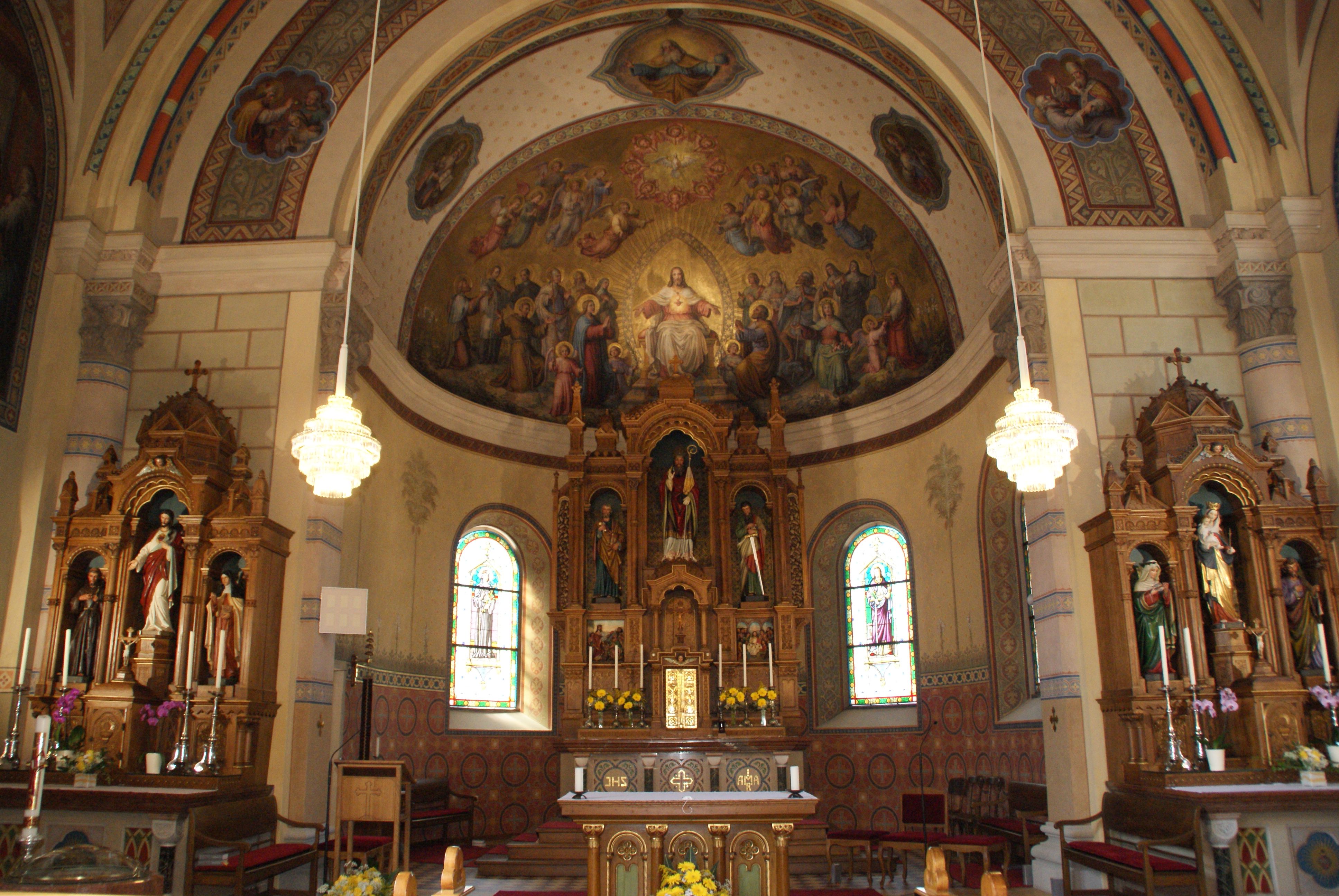 Interior view of a richly decorated church with altar, statues of saints and murals.