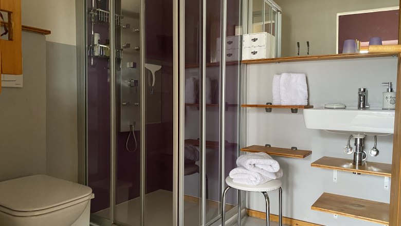 Modern bathroom with shower, washbasin, towels and shelves.