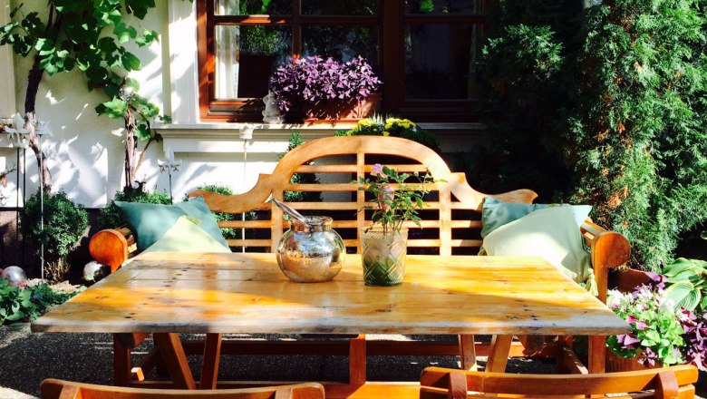 Cozy garden area with wooden table and chairs, surrounded by plants and vines.