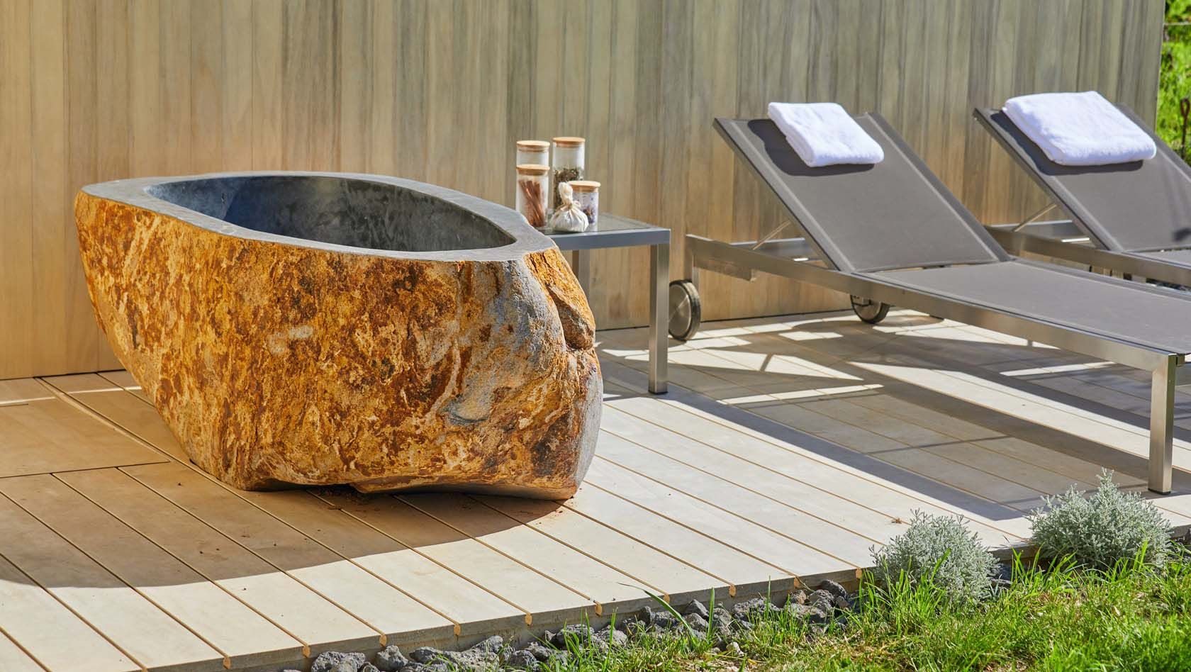 Stone bathtub and sun loungers on the outdoor wooden terrace.