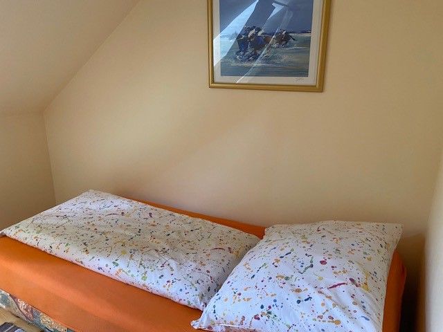 A bed with colorful bed linen in a single room, with a framed picture on the wall above it.