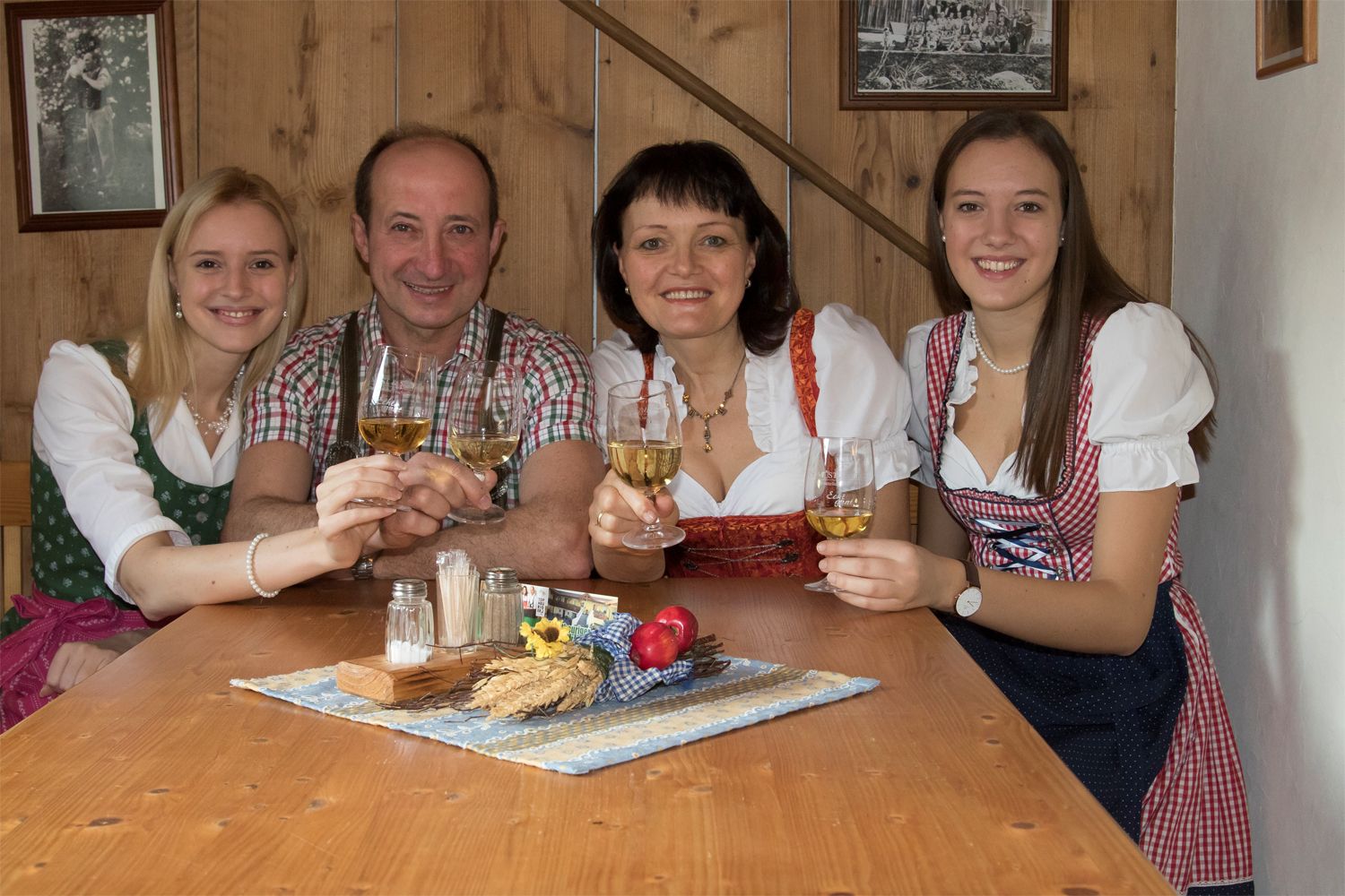 A family in traditional dress clinks glasses of wine at a wooden table.
