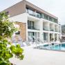 Modern building with pool and sun loungers, surrounded by green countryside and a castle in the background.