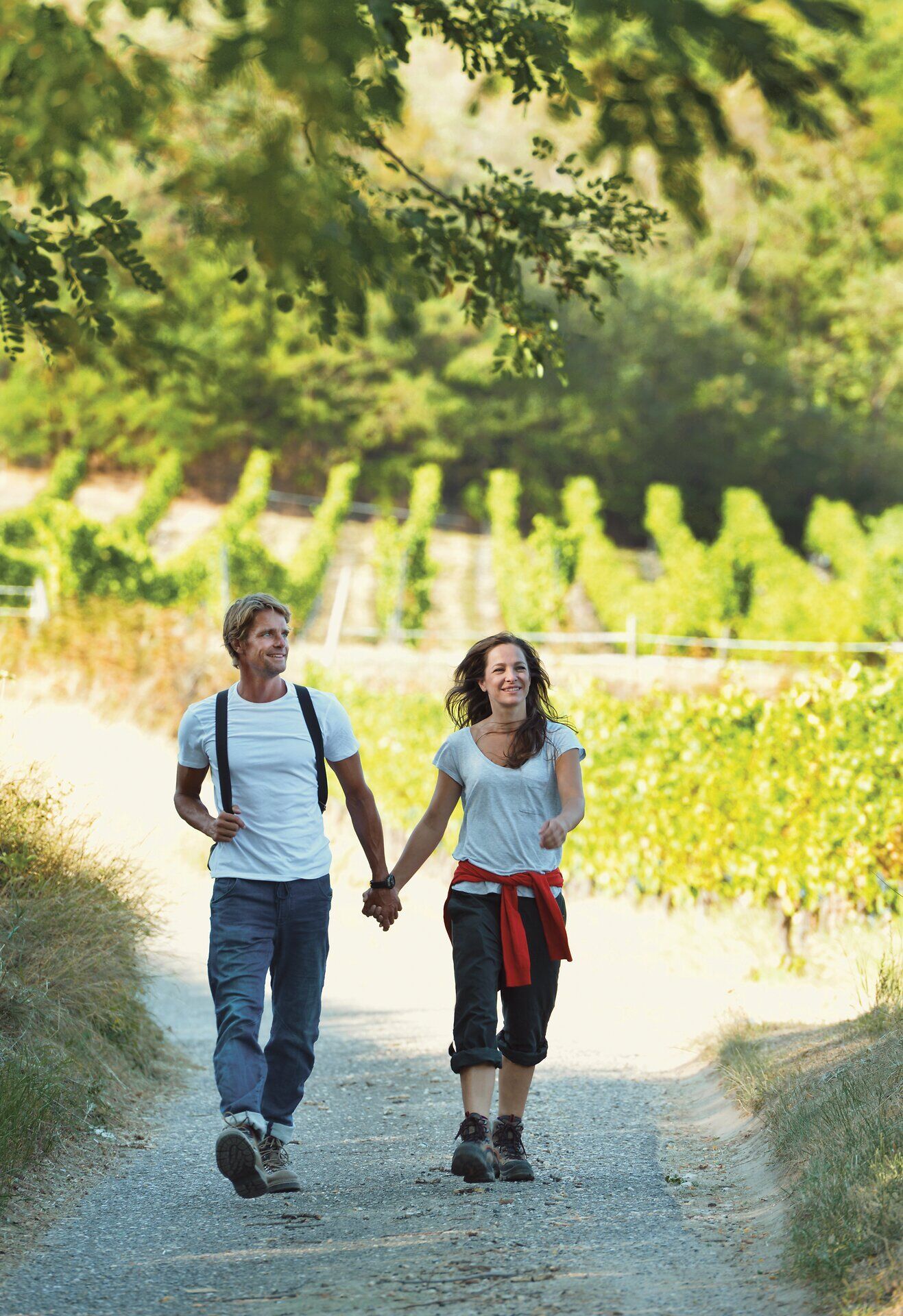 A couple walks along a gravel path. Vines can be seen in the background. 