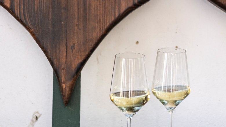 Two wine glasses with white wine on a wooden table in front of a heart-shaped wooden decoration.