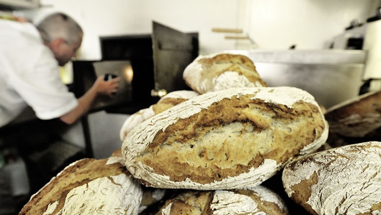 Freshly baked bread in front of a baker operating an oven.