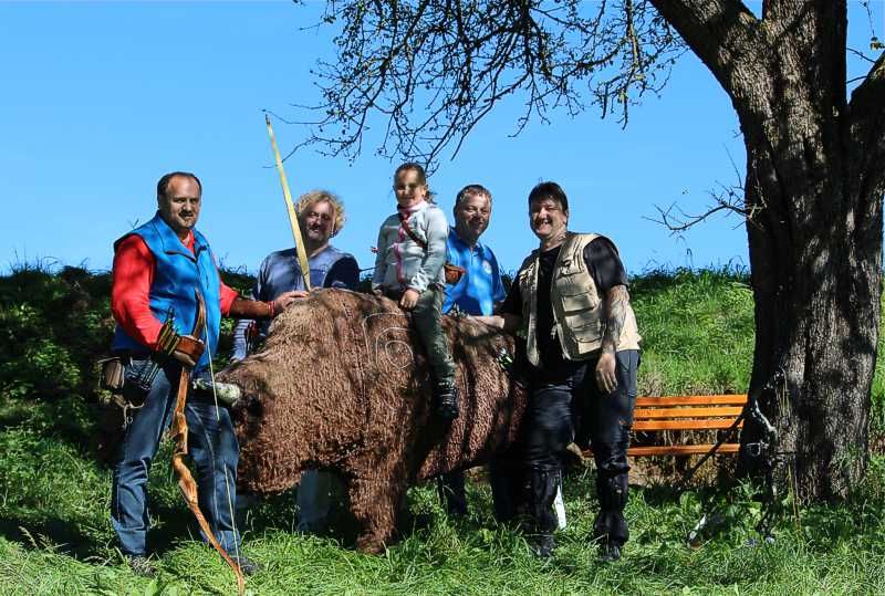 Group of people posing with an archery target in the shape of a bear outdoors.