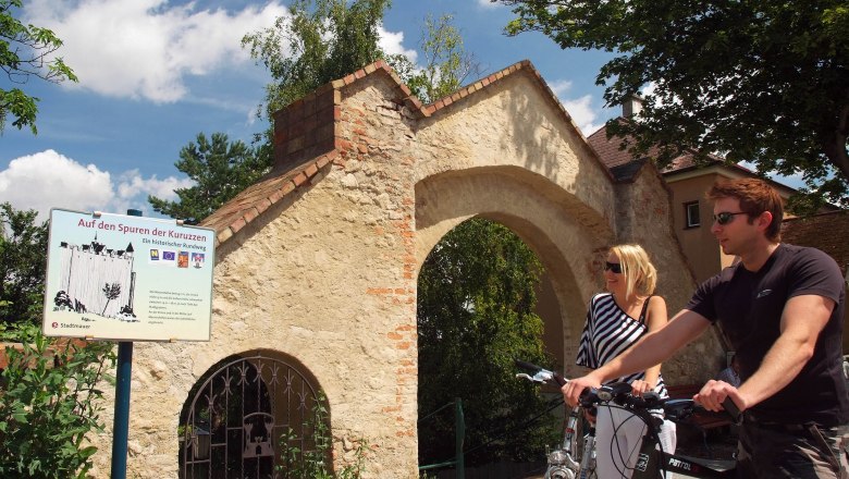 Two people with bicycles in front of a historic archway in Zistersdorf.