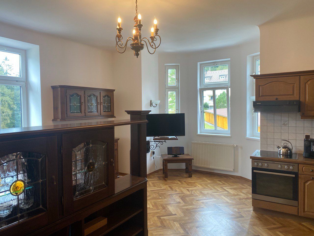Interior view of a kitchen with wooden furniture, a chandelier and large windows.