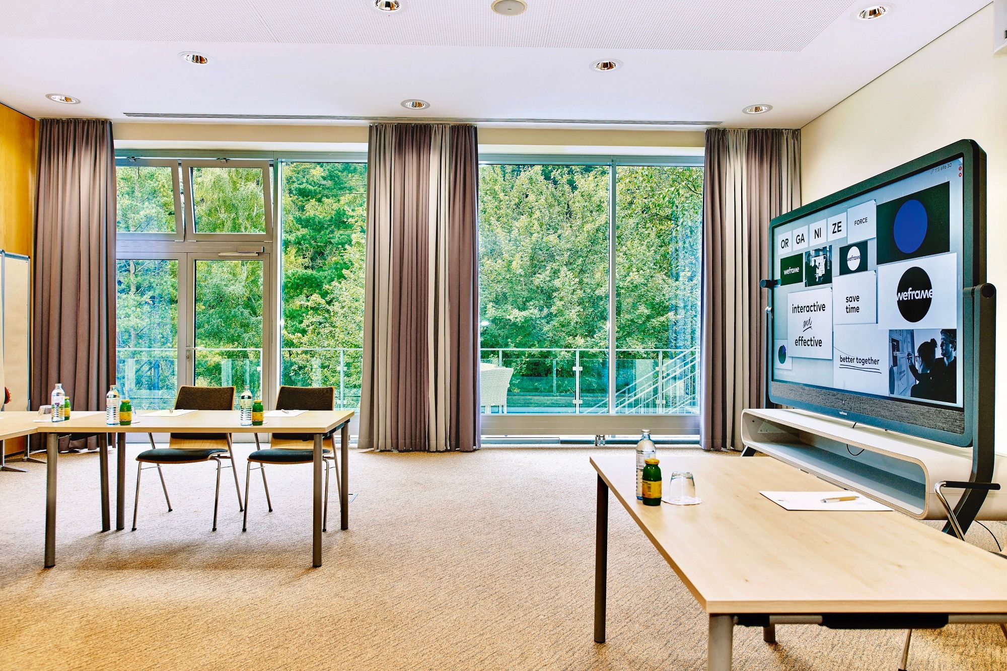 Modern seminar room with large windows, tables, chairs and an interactive screen.