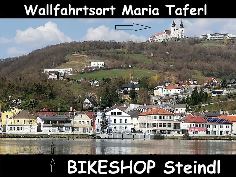View of Maria Taferl with church on a hill, below the village and a sign for the Steindl bike store.