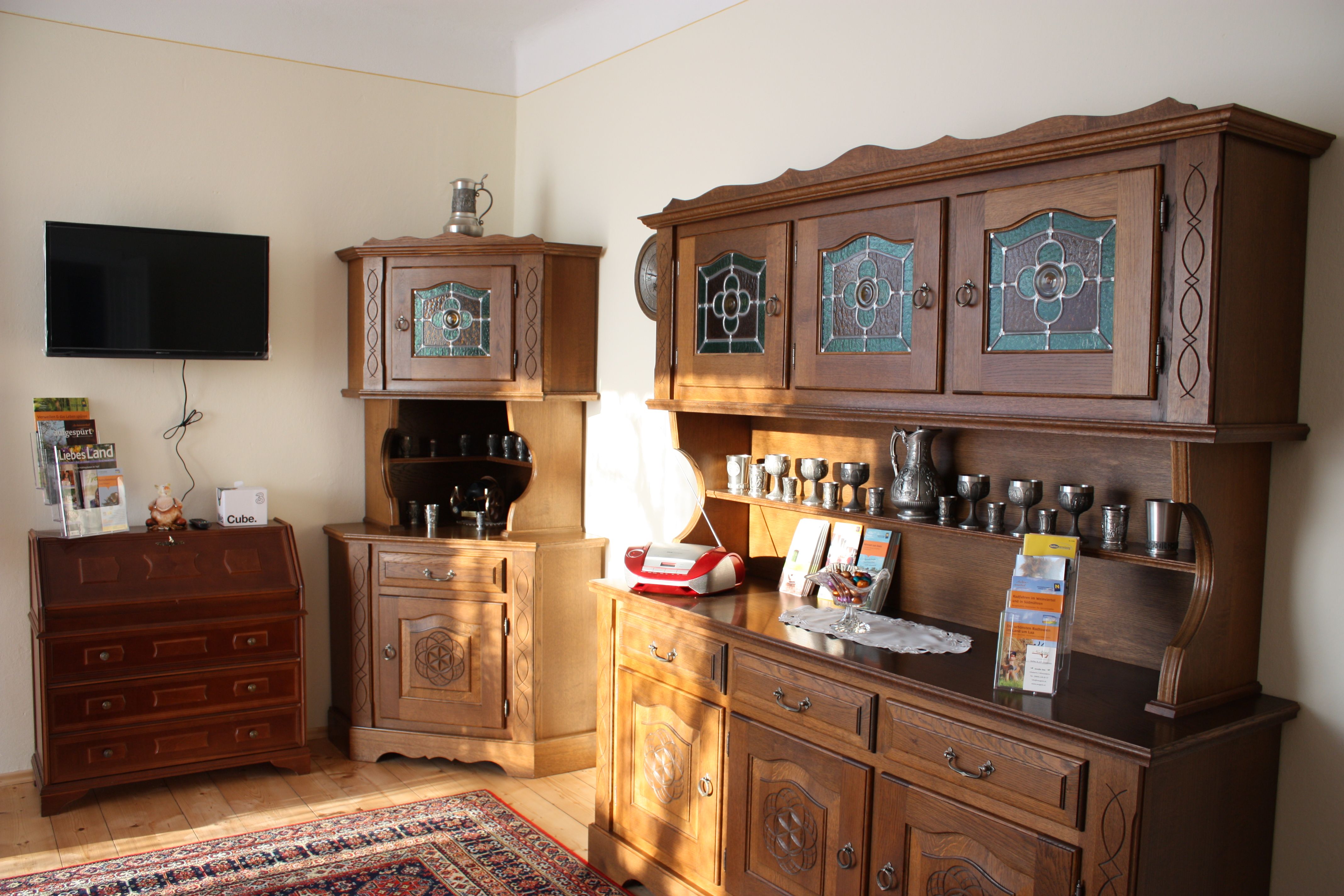 Living room with antique wooden furniture, a TV on the wall and decorative metal vessels.