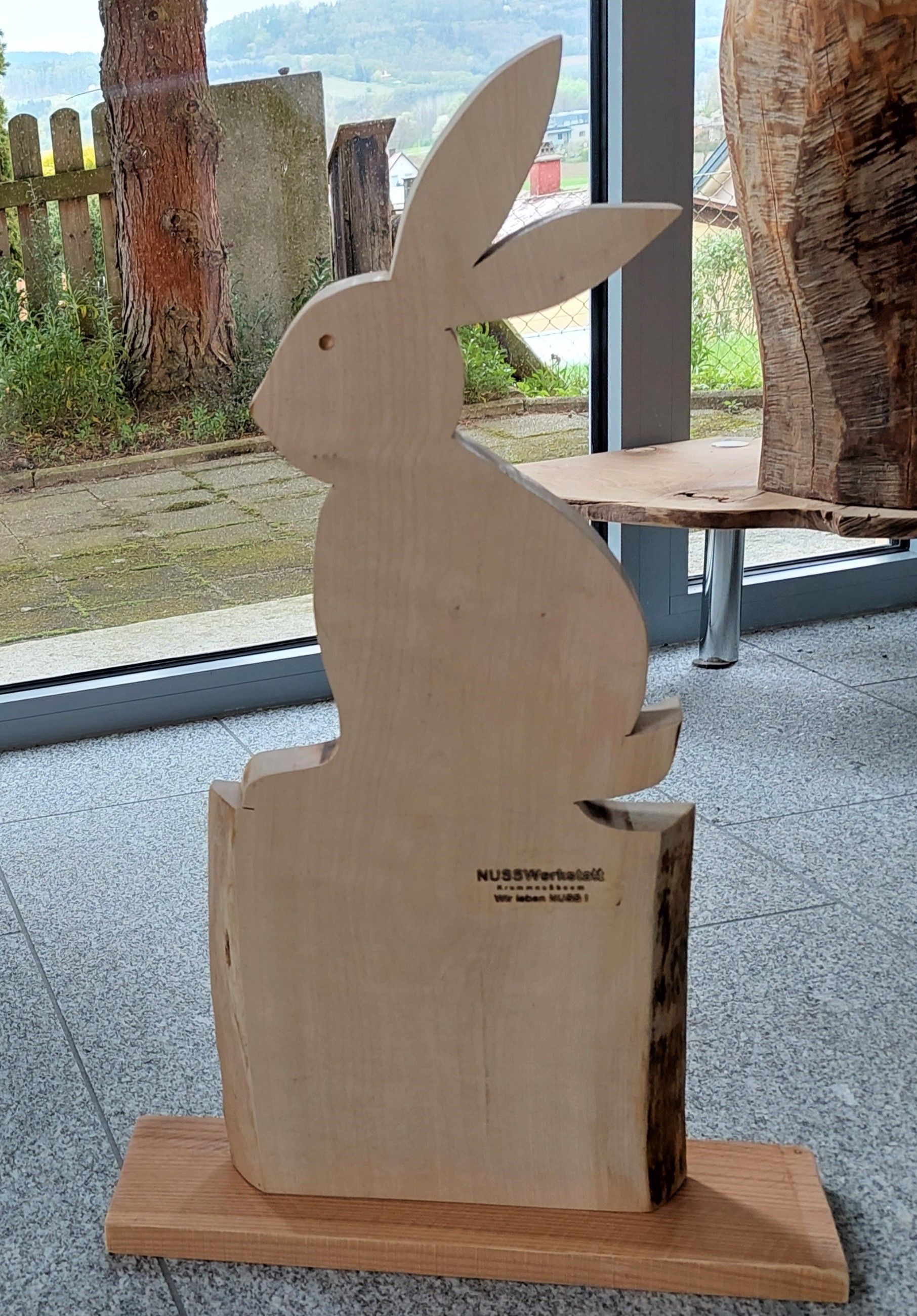 Wooden figure of a hare in front of a window with a view of a garden.