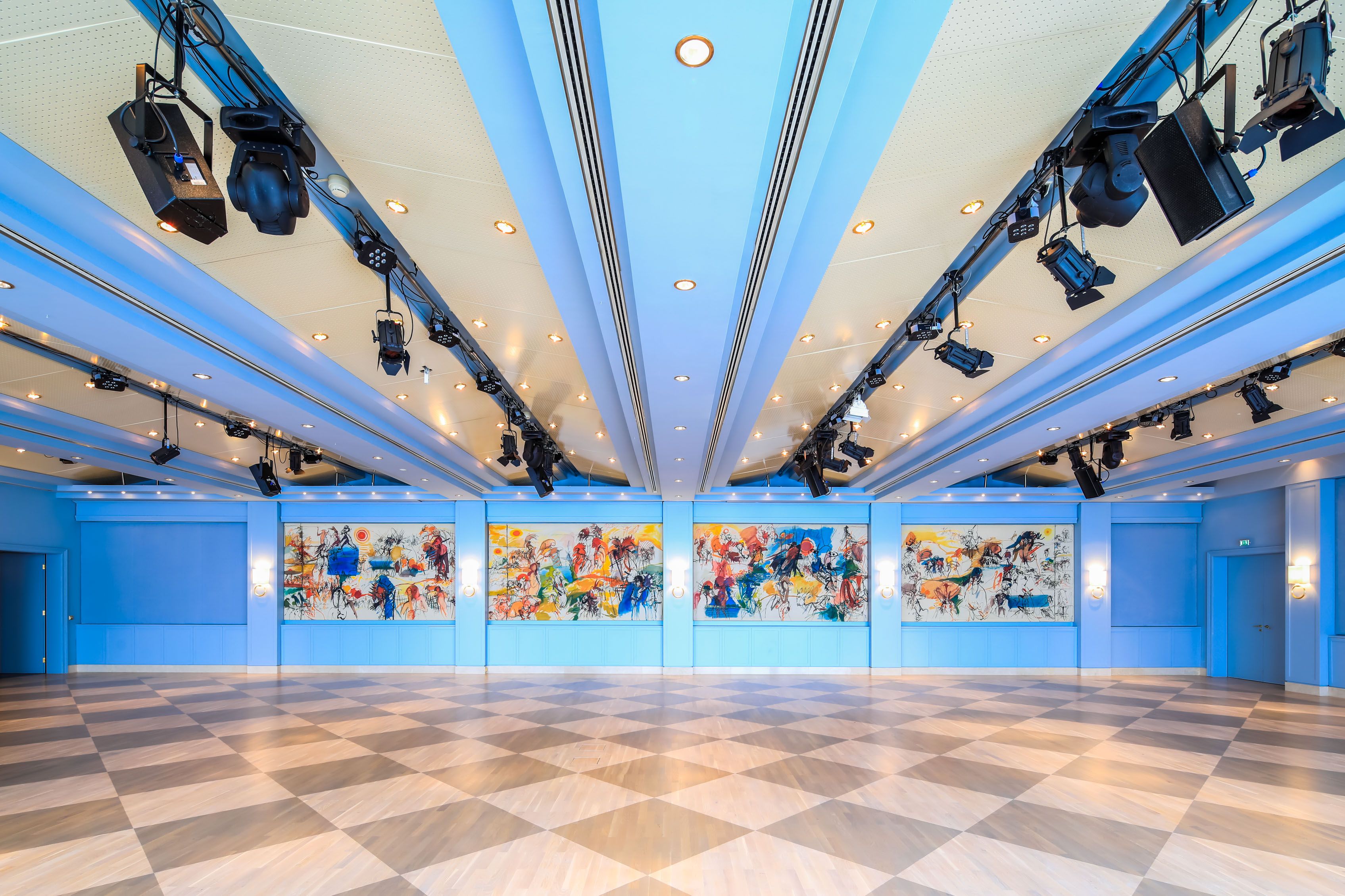Interior view of the Badener Saal in the Congress Center Baden with blue ceiling, colorful murals and diagonal floor tiles.