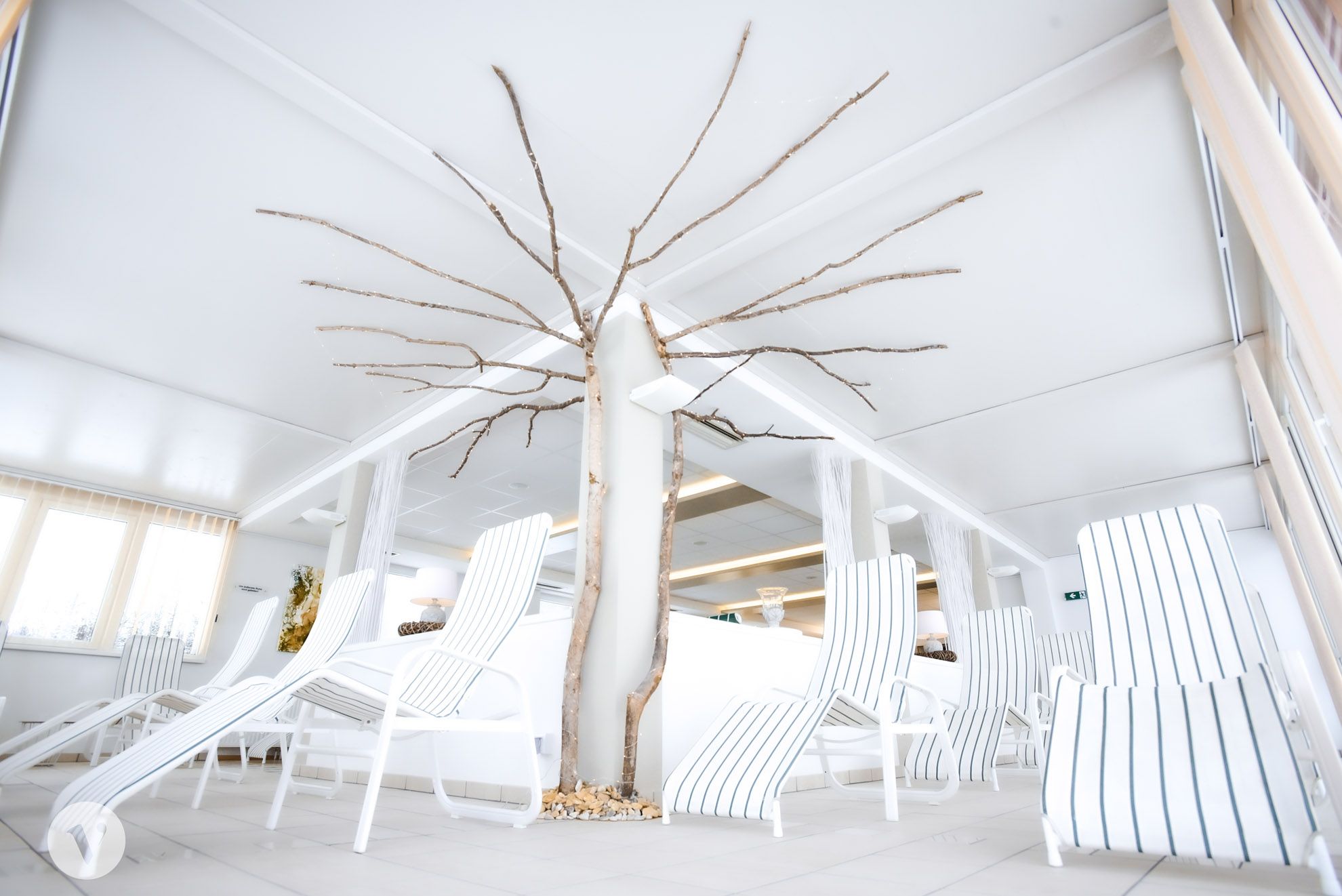 A bright relaxation area with white loungers and a decorative tree trunk in the middle.
