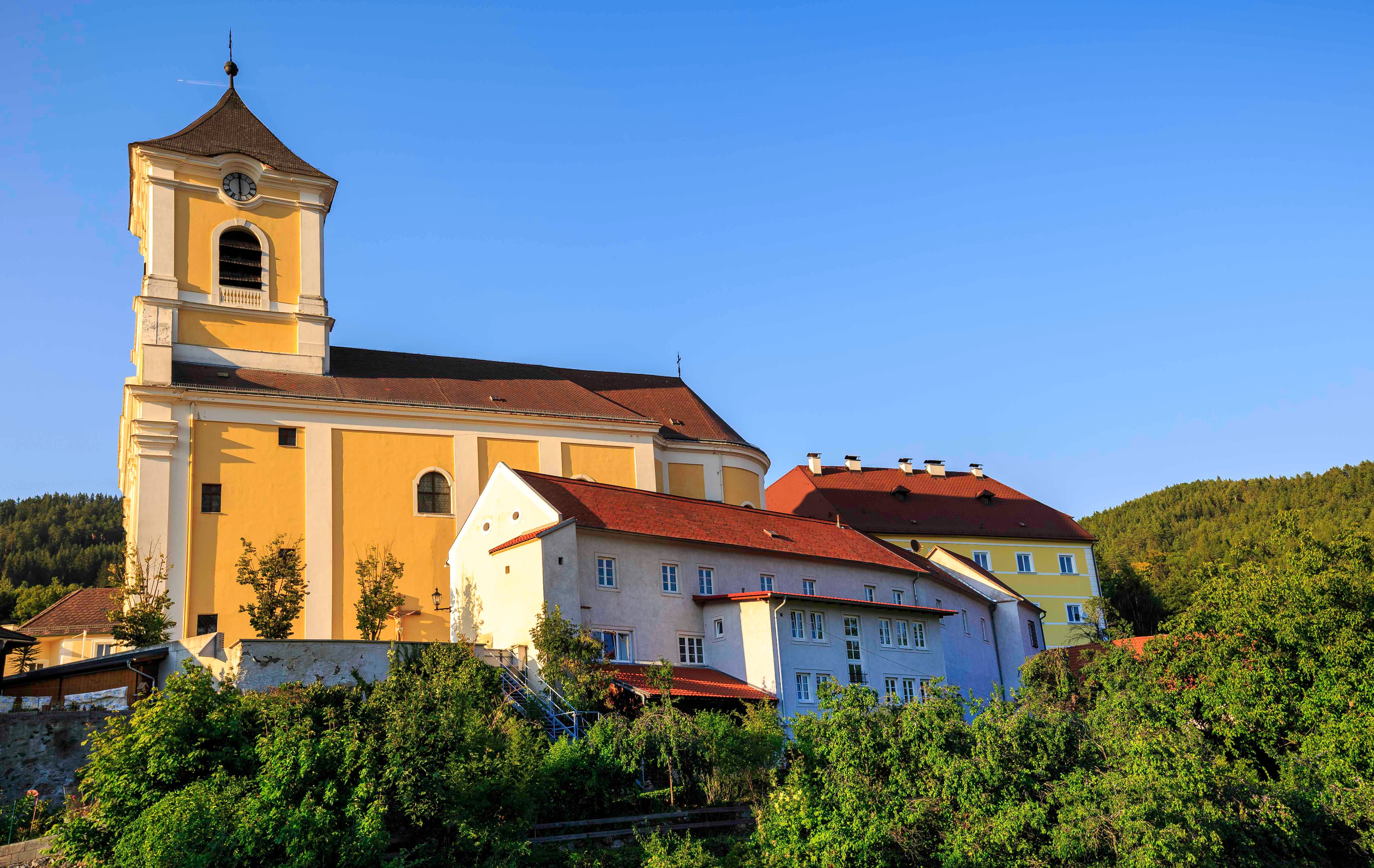 Parish church and monastery in a green landscape under a clear sky.