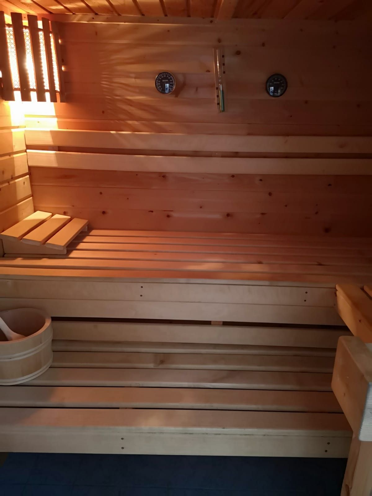 Interior view of a wooden sauna with benches, thermometer and bucket.