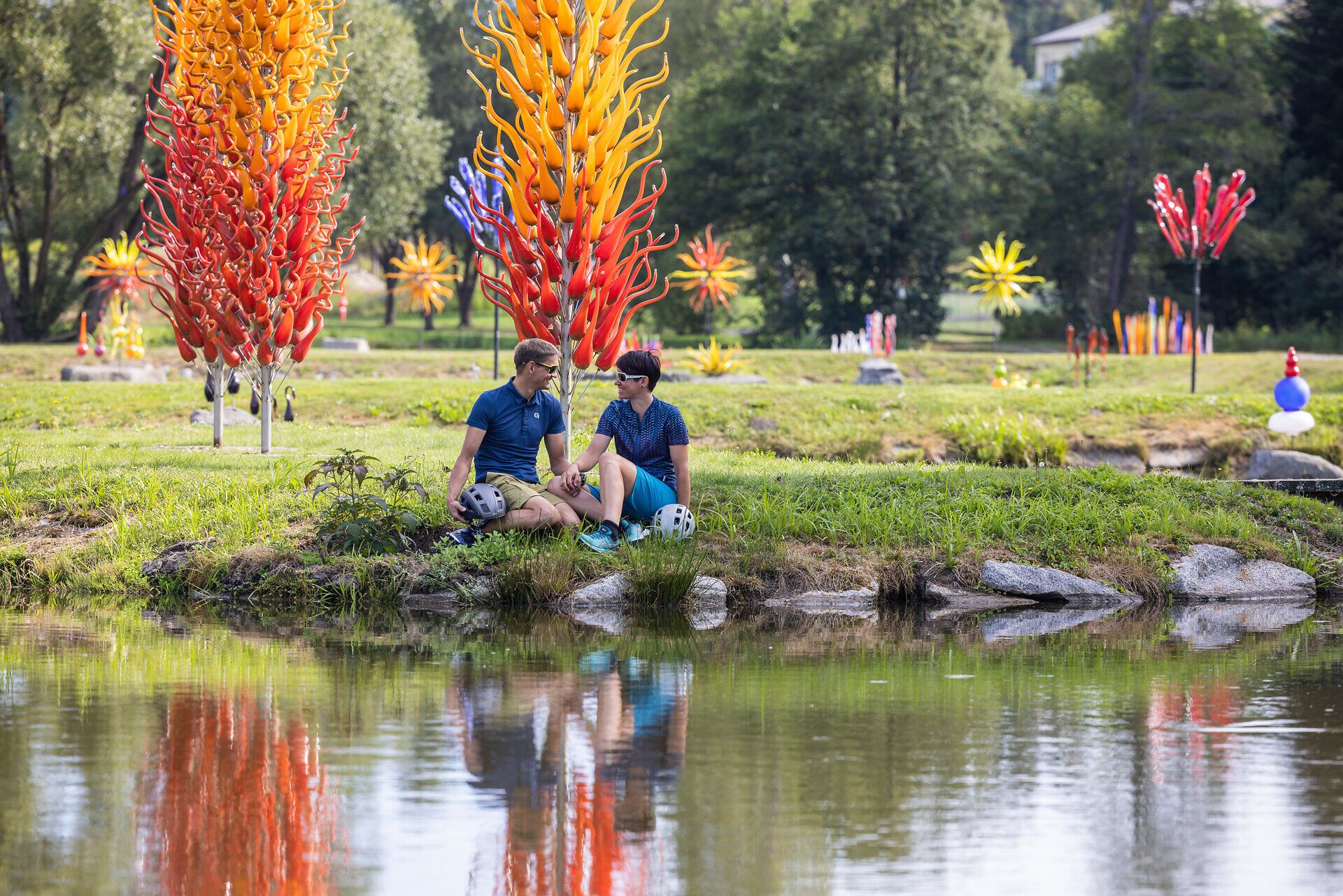 In the middle of a fascinating water landscape, two cyclists relax on the shore, surrounded by luminous works of glass art that shine in the sun. The harmonious combination of art and nature creates an inviting atmosphere that invites you to linger and experience the beauty of the Waldviertel.