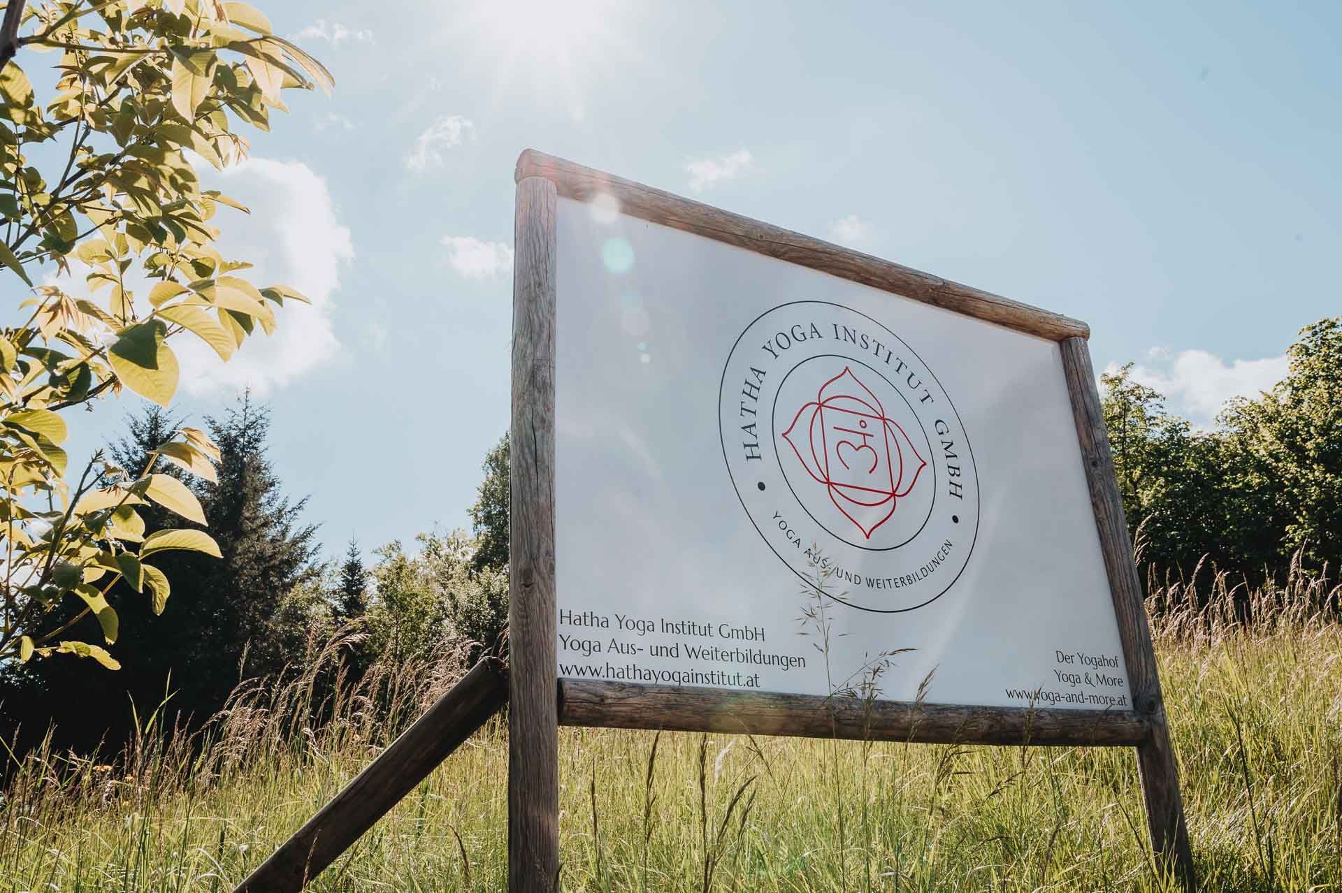 A sign for the Hatha Yoga Institute stands on a meadow under a sunny sky.
