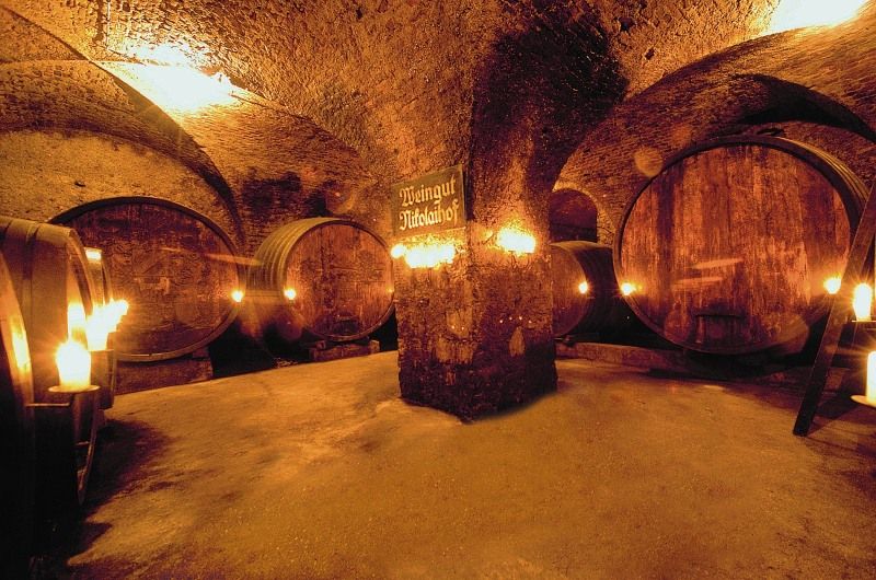 Historic wine cellar with large wooden barrels and candle lighting.
