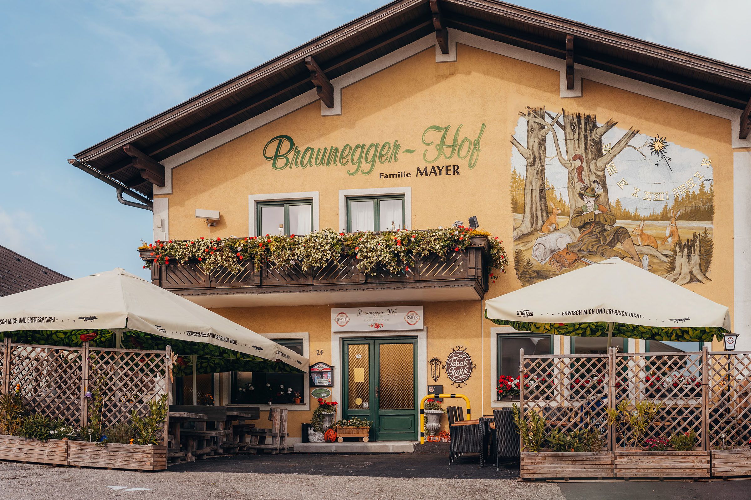 A traditional inn with a balcony and murals, surrounded by parasols and plants.