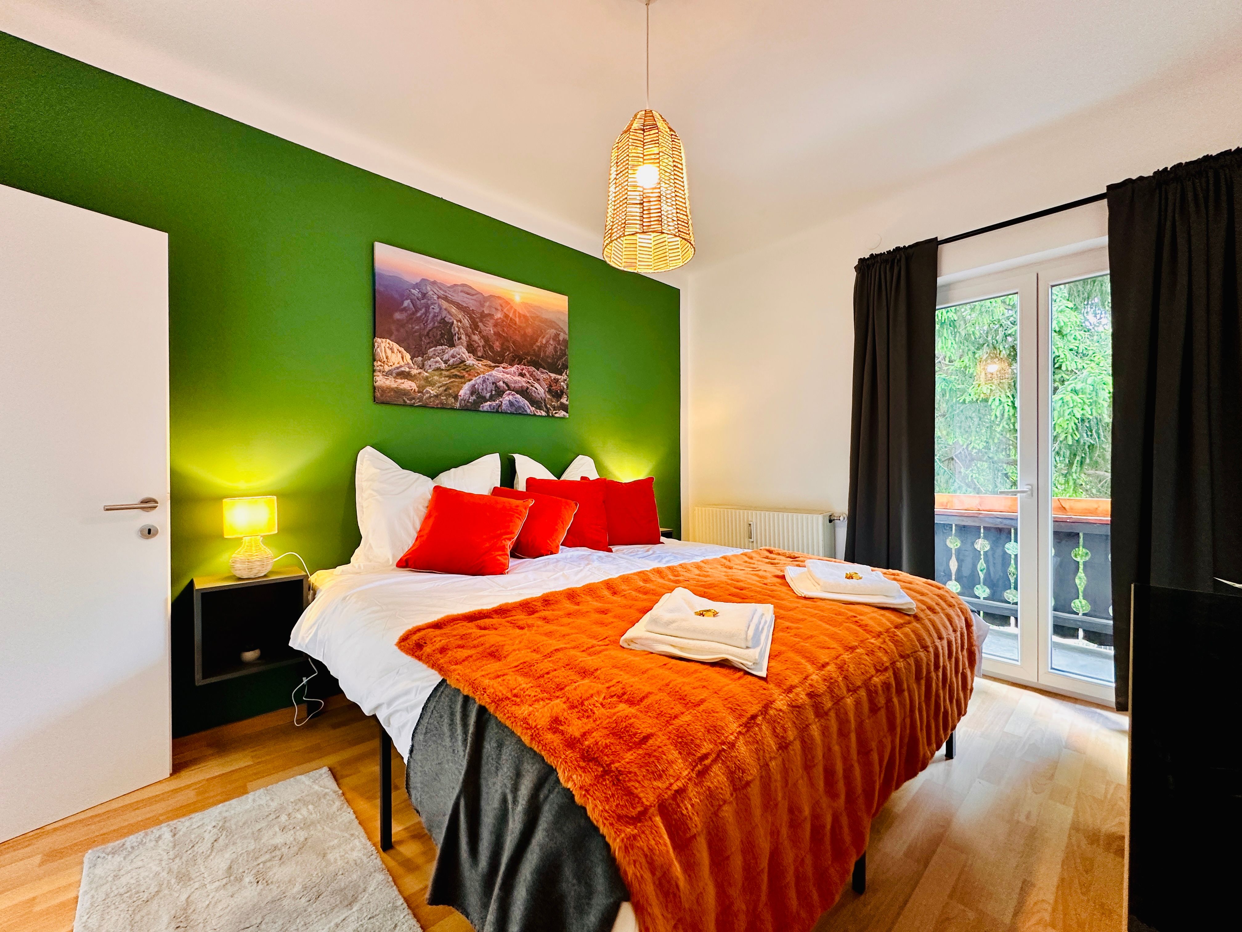 Cozy bedroom with green painted wall, double bed with orange blankets and pillows, lamp and balcony.