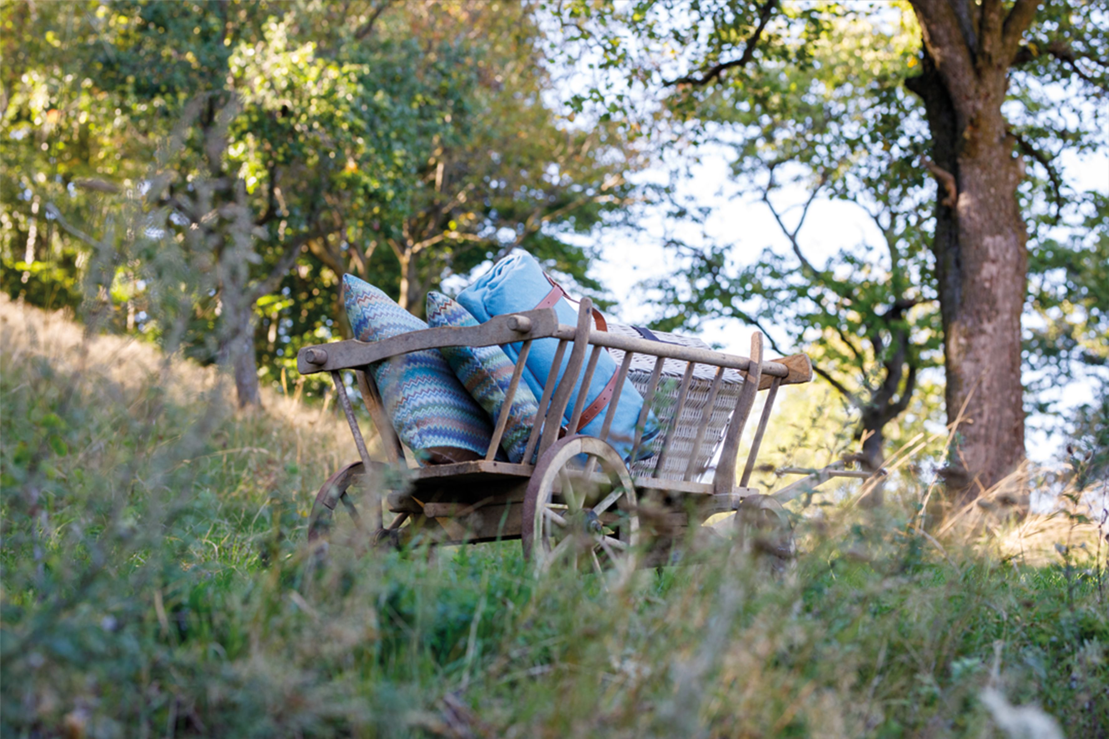 A wooden wagon with pillows and blankets is parked in a meadow in the forest.