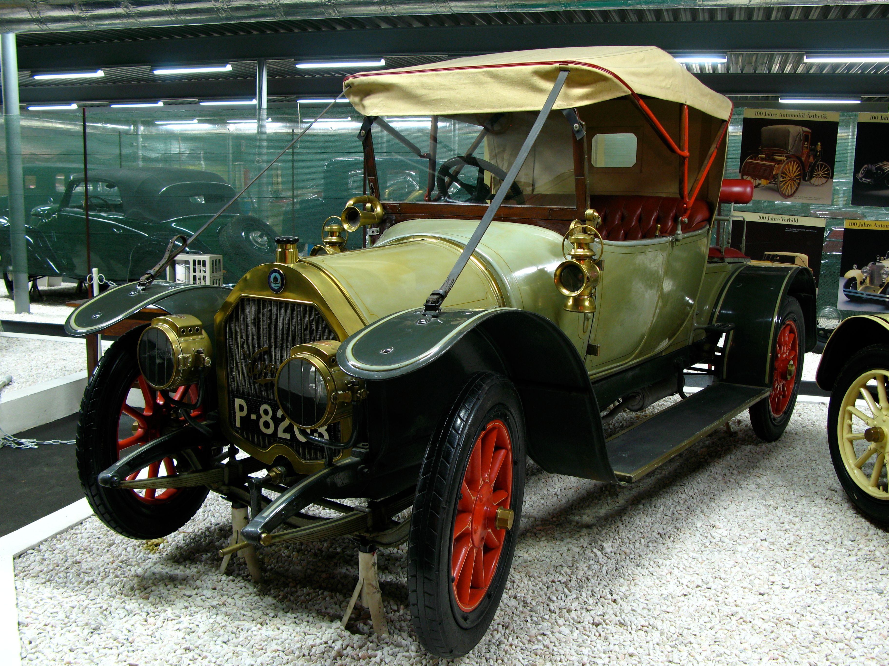 A vintage car with a red top and red wheels in an automobile museum.
