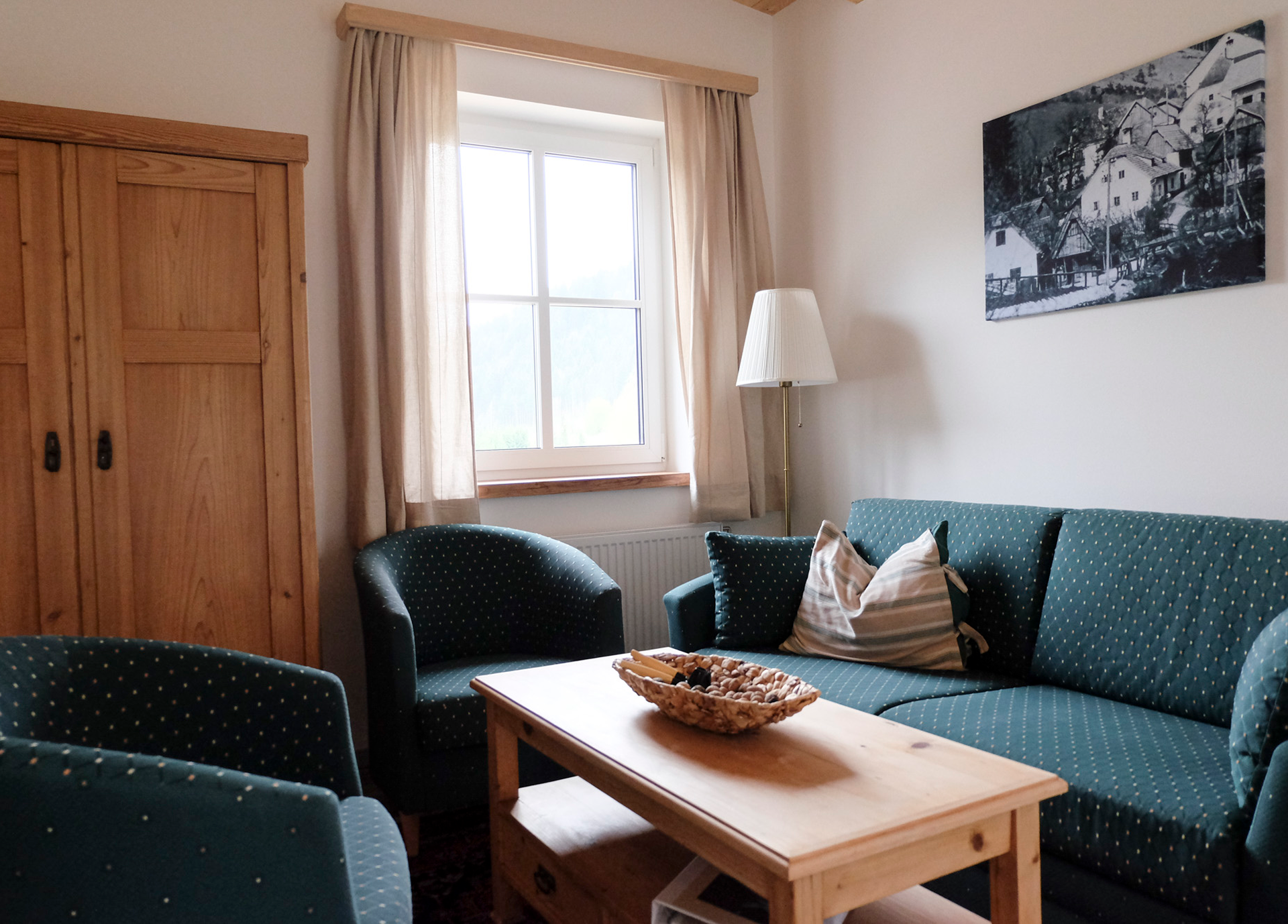 A cozy living room with green upholstered furniture, a wooden table, and a window with curtains.