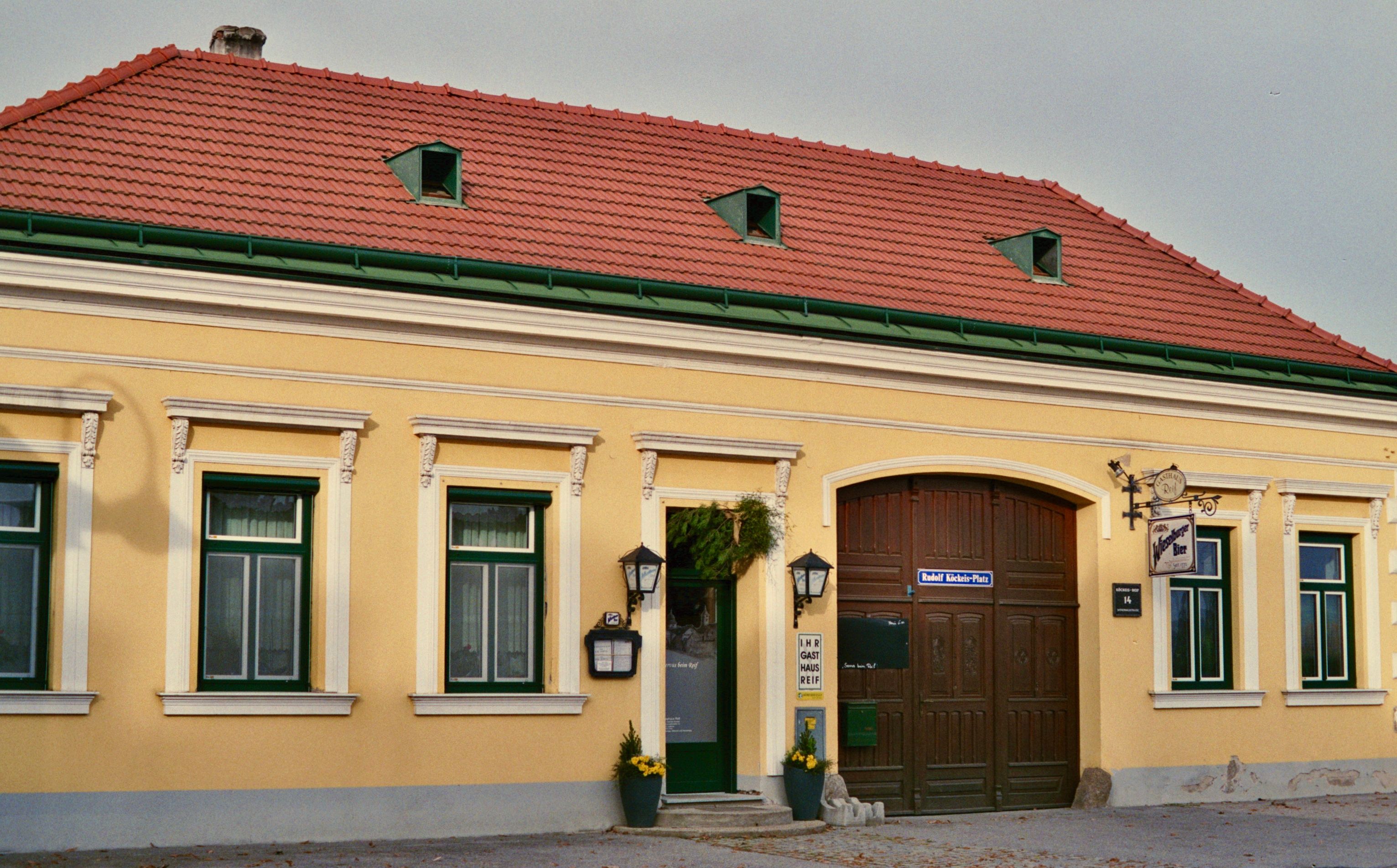 Exterior view of a yellow inn with red roof tiles and green window frames.