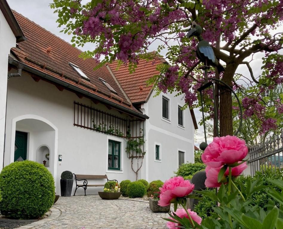 A country house with red roof tiles, surrounded by blossoming trees and pink flowers in the foreground.