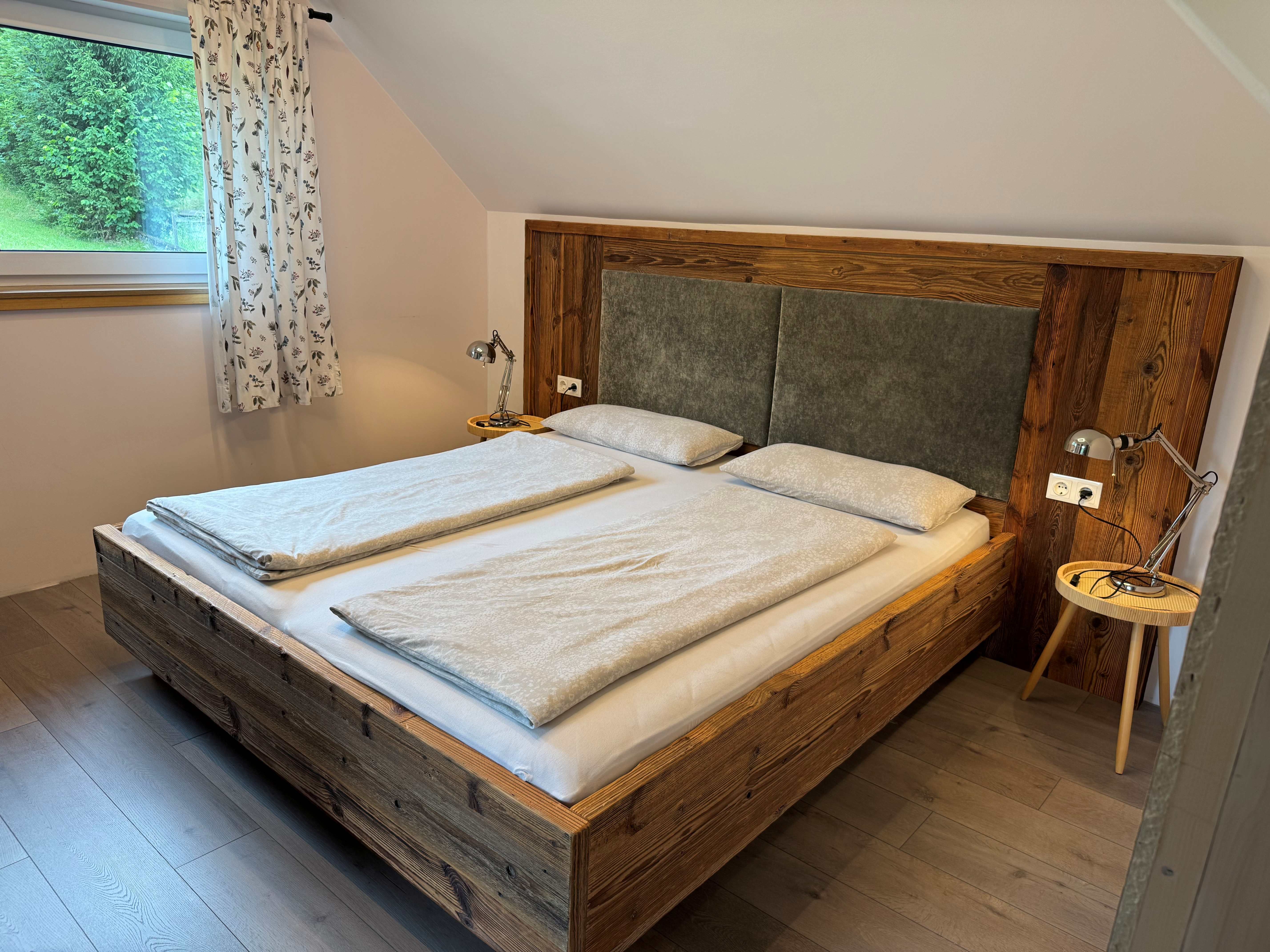 A cozy bedroom with a wooden double bed, two nightstands with lamps, and a window with curtains.