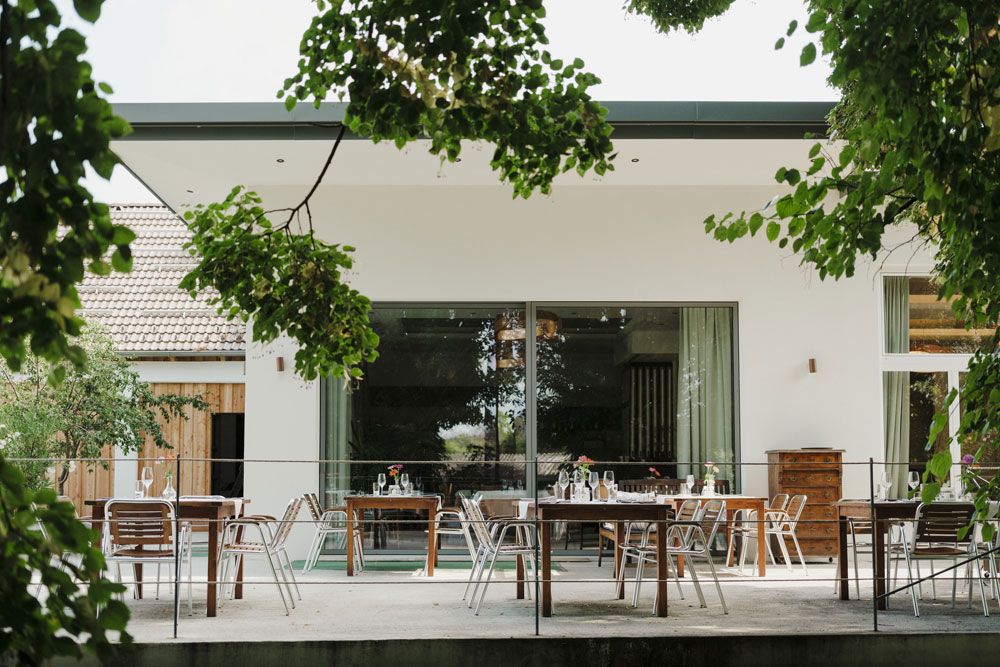 Terrace with tables and chairs, surrounded by green trees.