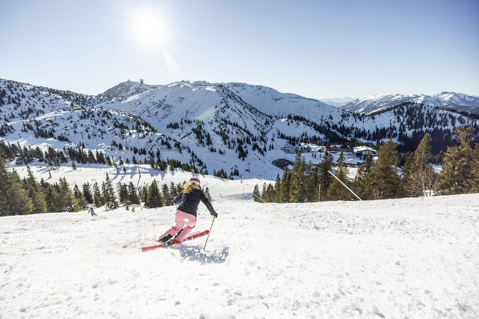 Die strahlende Sonne glitzert auf der unberührten Schneedecke, während eine Skifahrerin elegant die Piste hinuntergleitet. Umgeben von majestätischen Bergen und dichten Nadelwäldern, bietet dieser Ort ein wahres Winterparadies für alle Wintersportliebhaber.