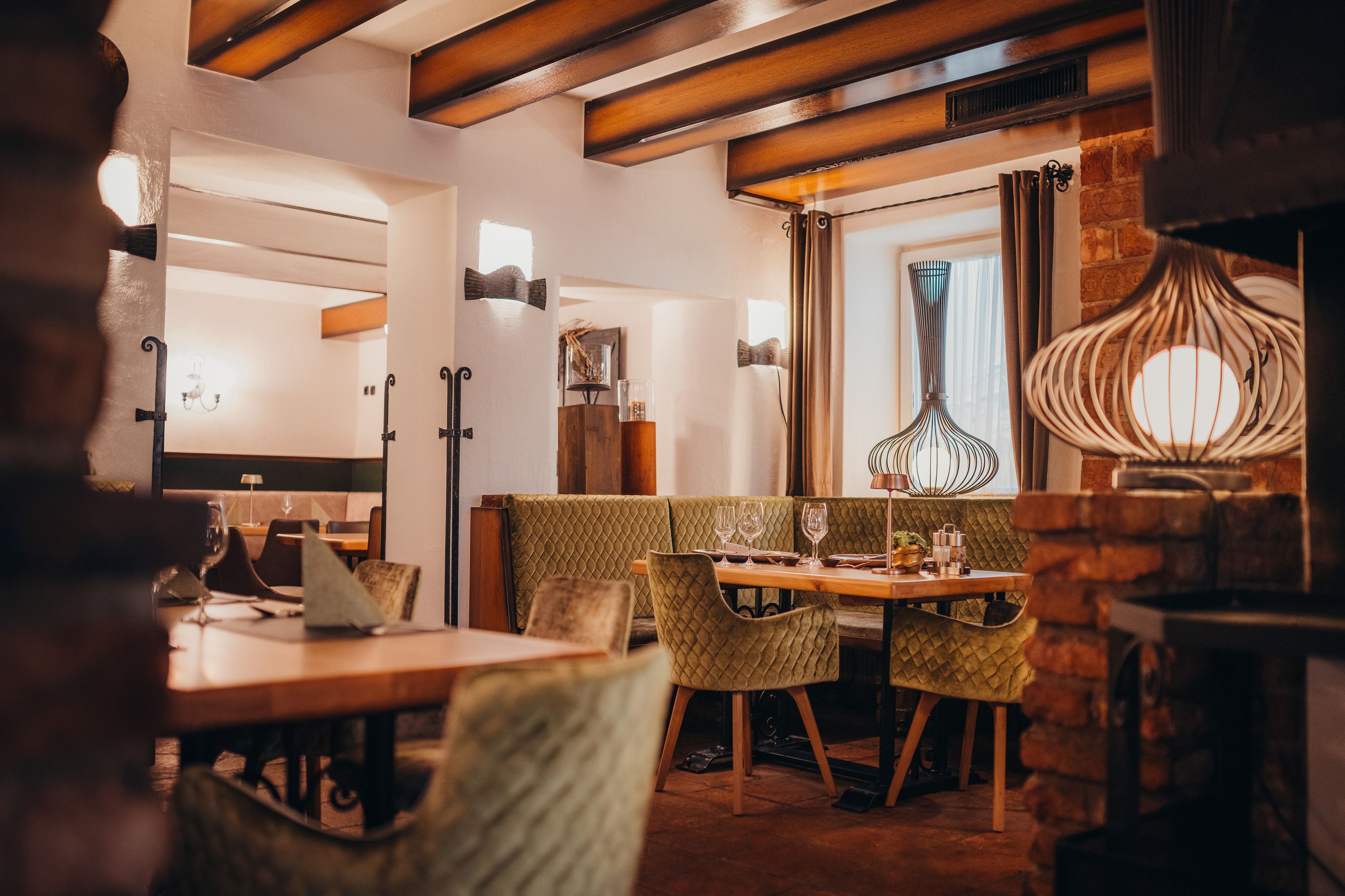 Cozy restaurant with wooden beams, green upholstered chairs and decorative lamps.