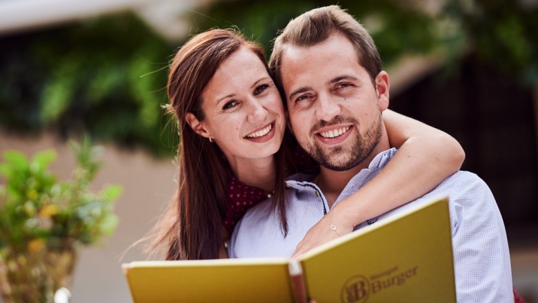A smiling couple holding a menu card at the wine tavern Burger.