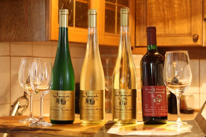 Four wine bottles and glasses on a table in a kitchen.
