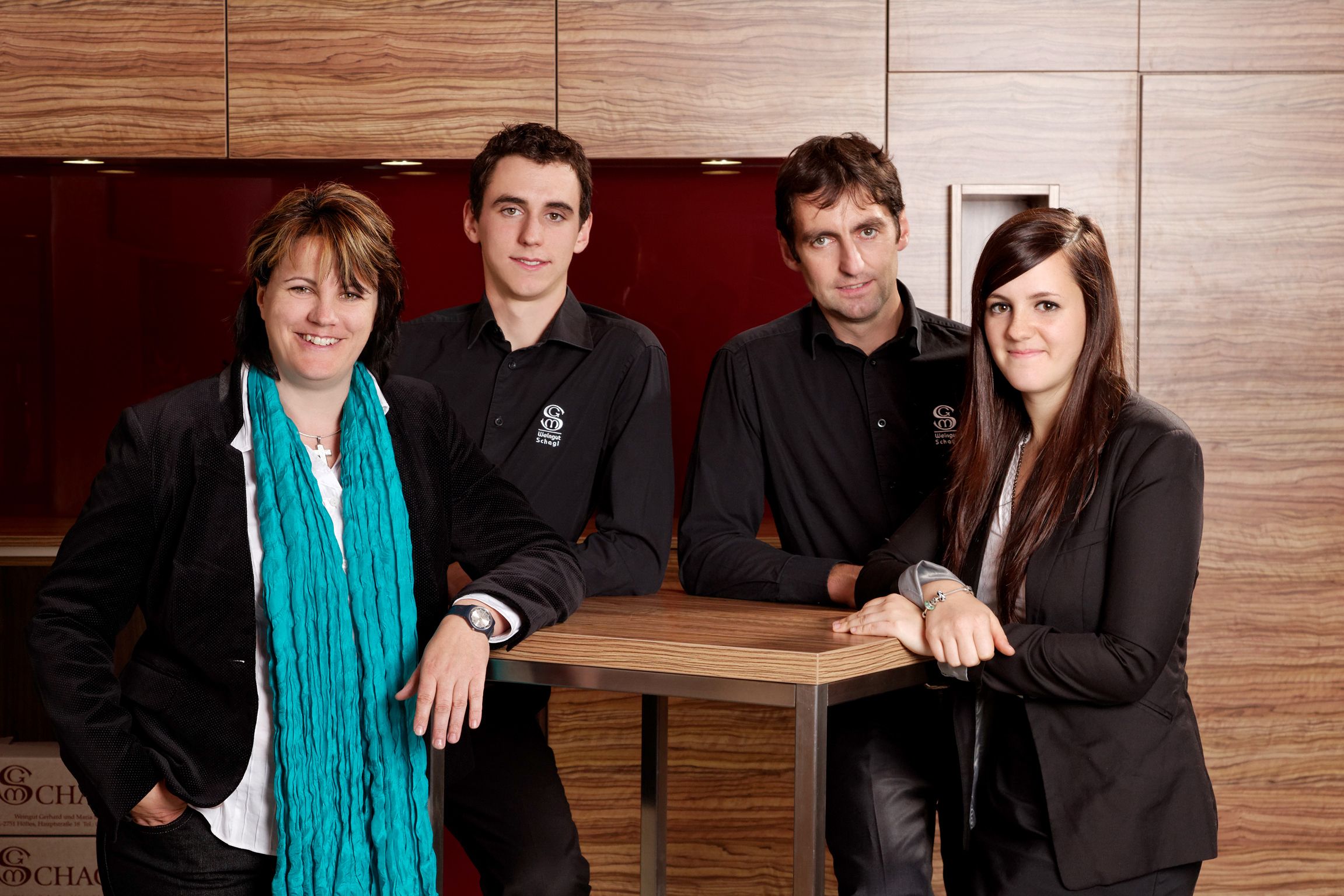 Four people stand smiling in front of a wooden wall.