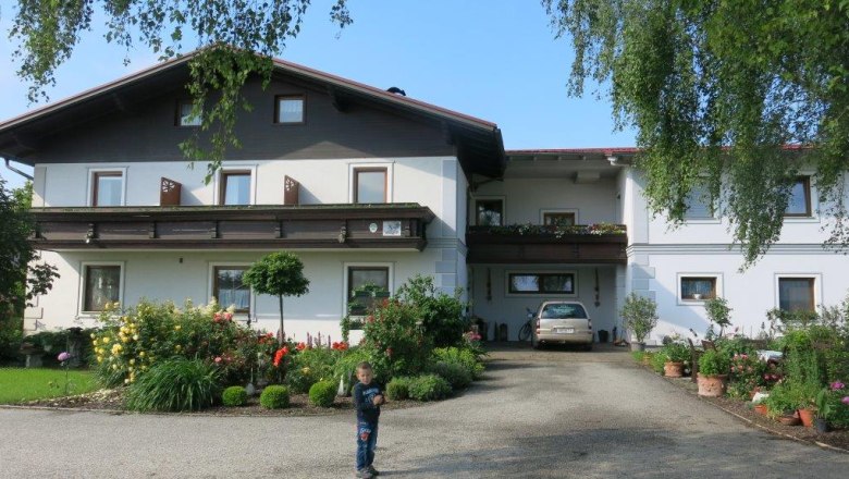 A traditional guest house with balcony, surrounded by a well-tended garden. A child stands on the path in front of the house.