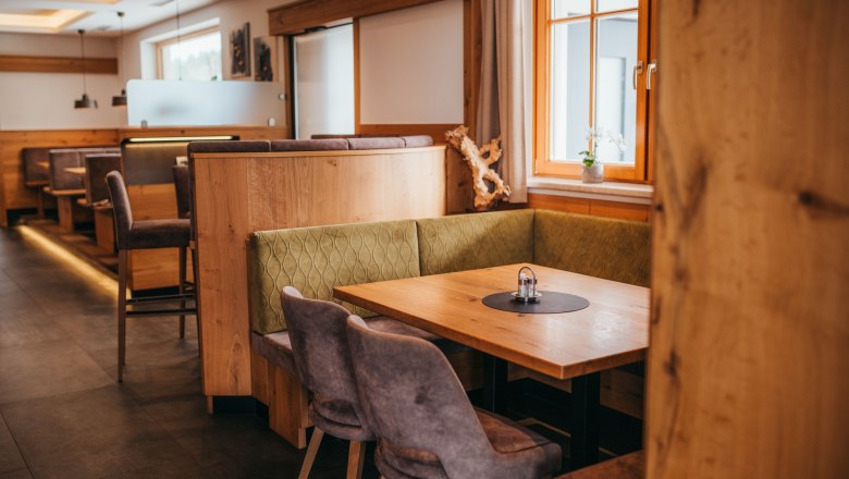Cozy dining room with wooden furniture and upholstered benches, windows with curtains, table with salt and pepper shakers.