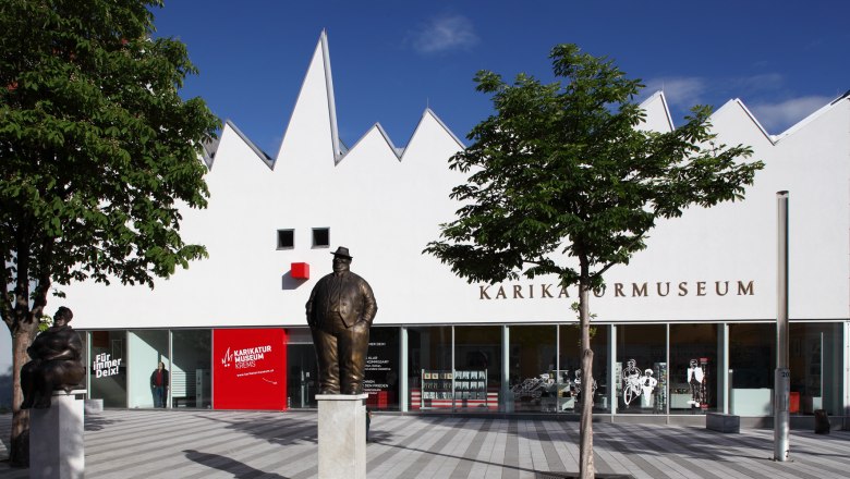 Exterior view of the Caricature Museum Krems with statues and trees.