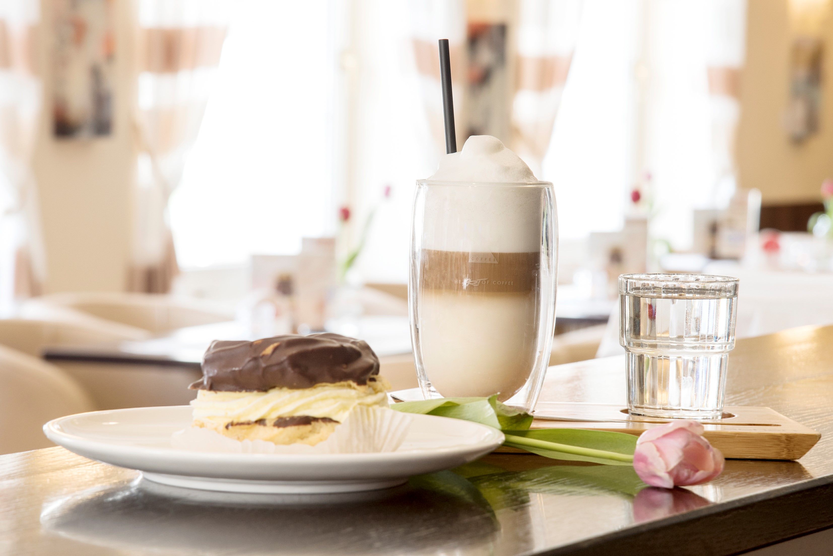A plate with a chocolate dessert, a latte macchiato and a glass of water on a table in a café.