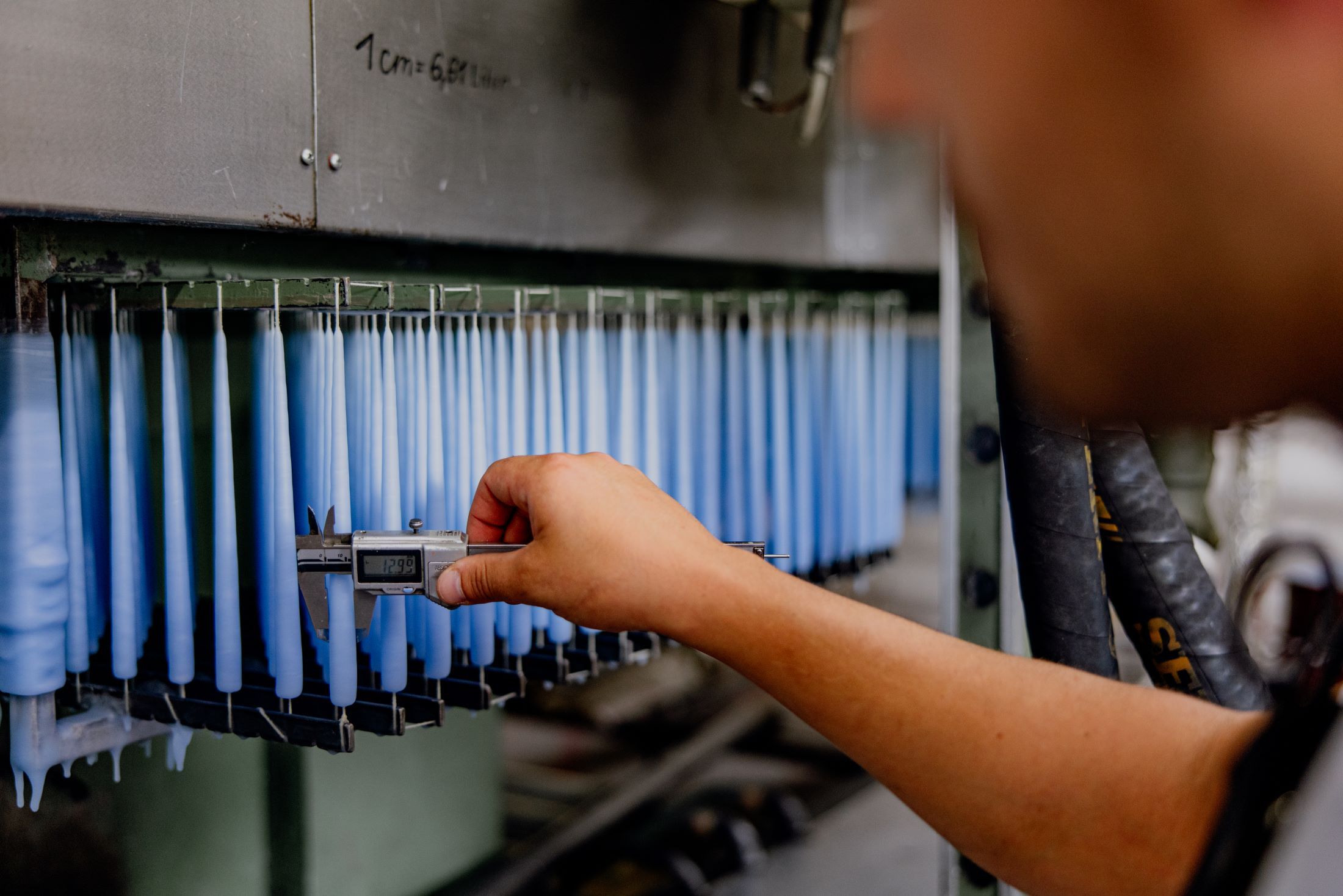 A person measures the thickness of blue candles with calipers in a factory.