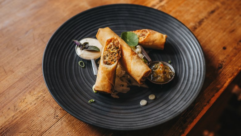 Fried spring roll with bacon cabbage and wasabi served on a black plate.