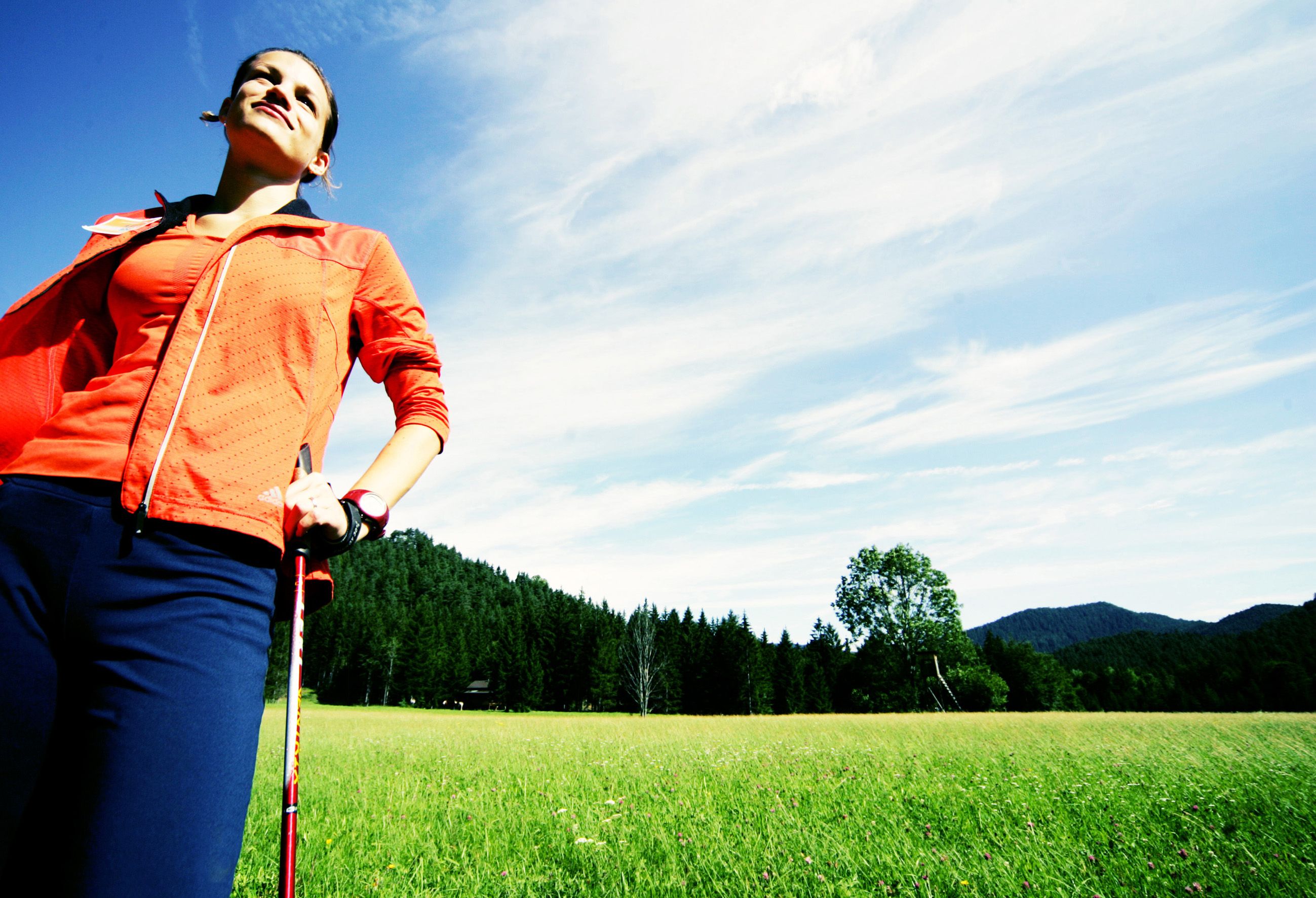 Woman in sportswear with Nordic walking poles on a meadow in front of a forest.