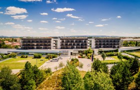 Exterior view of the Therme Laa Hotel with green garden and blue sky.