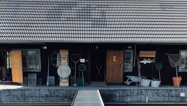 A fisherman's house with wooden doors and fishing nets on the wall, with a jetty over the water in front of it.
