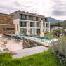 Exterior view of a modern boutique hotel with pool and sun loungers, surrounded by green countryside and hills.